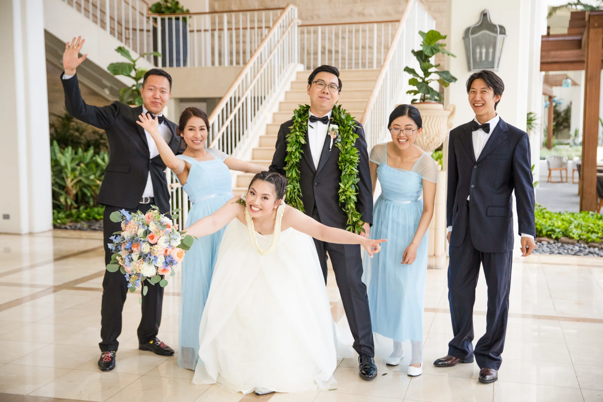 Elegant bridal party at Four Seasons Oahu, featuring bride in white dress and groom with lei, holding vibrant bouquet.