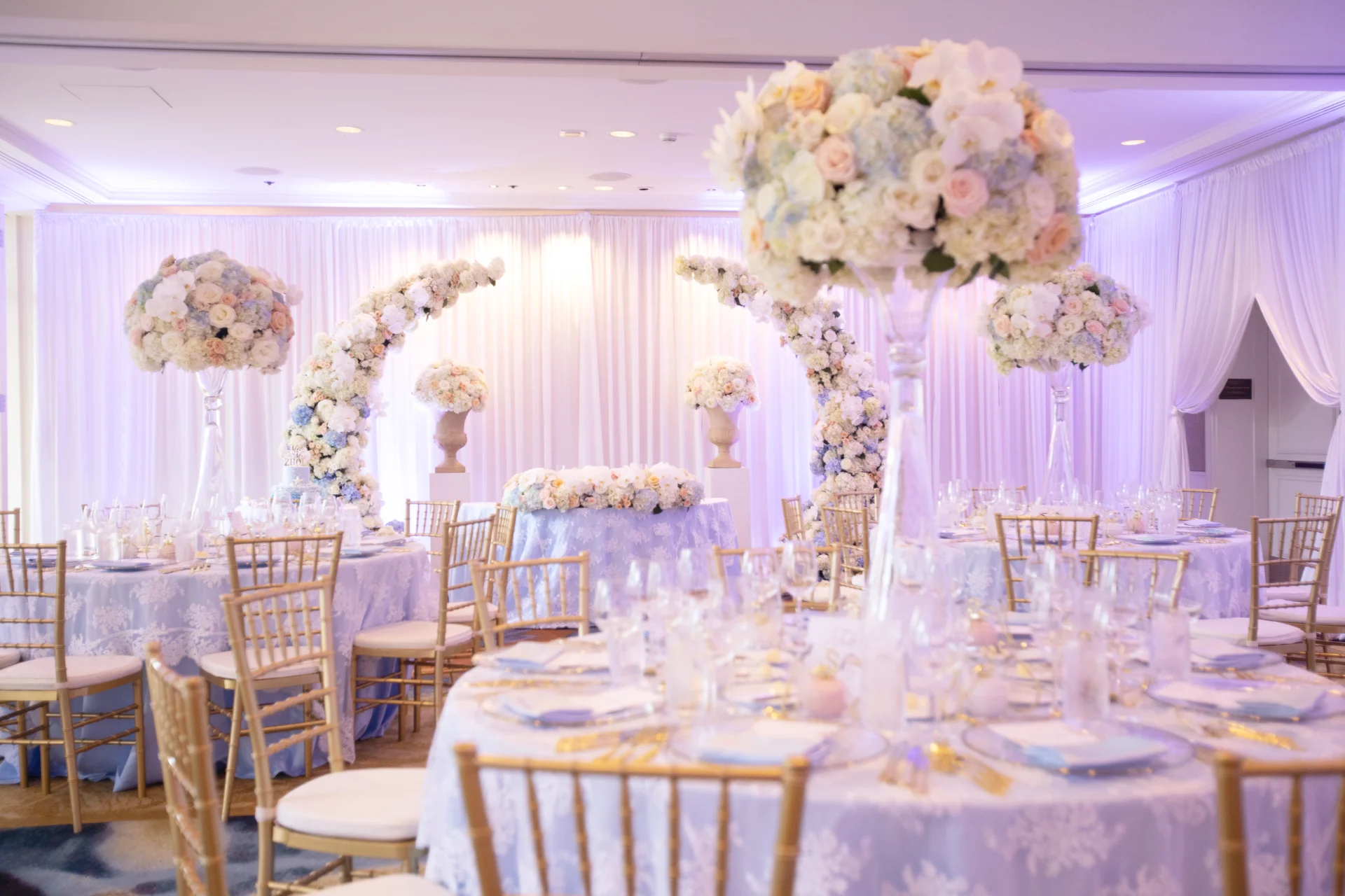 Elegant wedding reception at Four Seasons Oahu with pastel floral centerpieces, gold chairs, and lavender lighting.