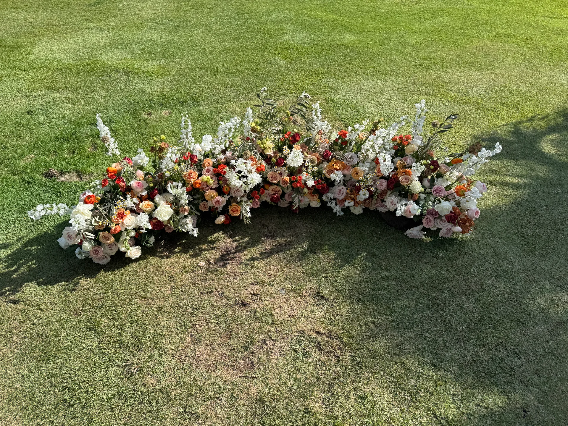 Lush floral arrangement on a grassy lawn, featuring roses and wildflowers in rich orange, pink, and white hues on Oʻahu.