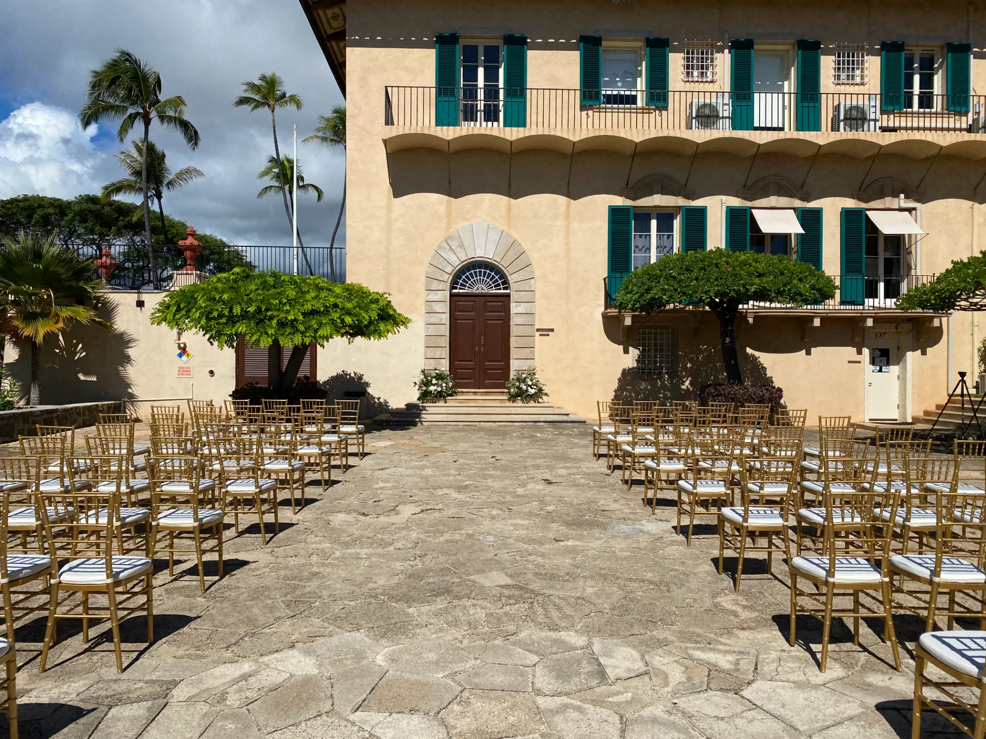 Outdoor wedding ceremony setup with gold chairs and a historic estate backdrop on Oʻahu, Hawaii.