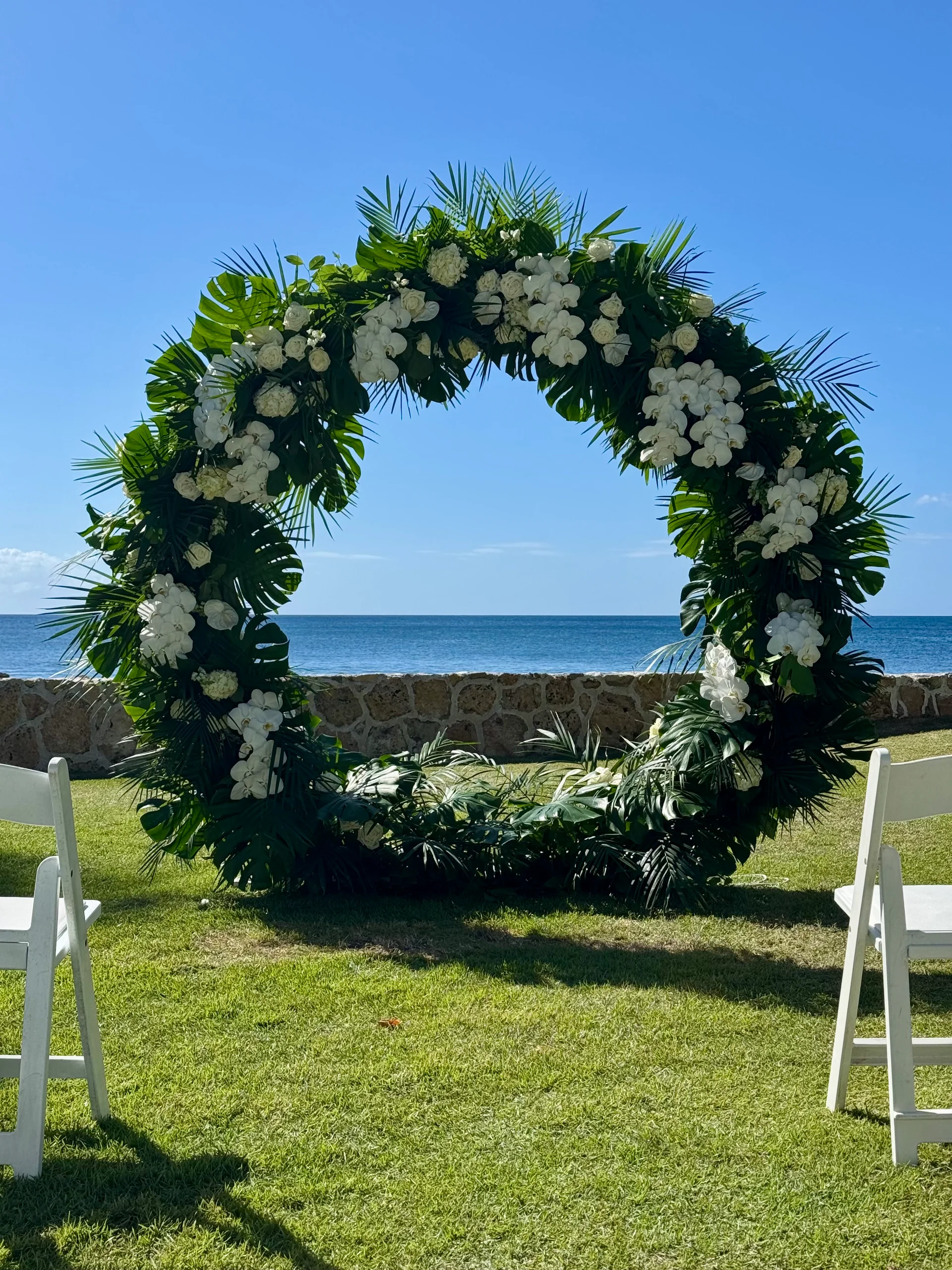 Floral circle arch with white orchids and greenery on beach lawn, Oʻahu wedding setting