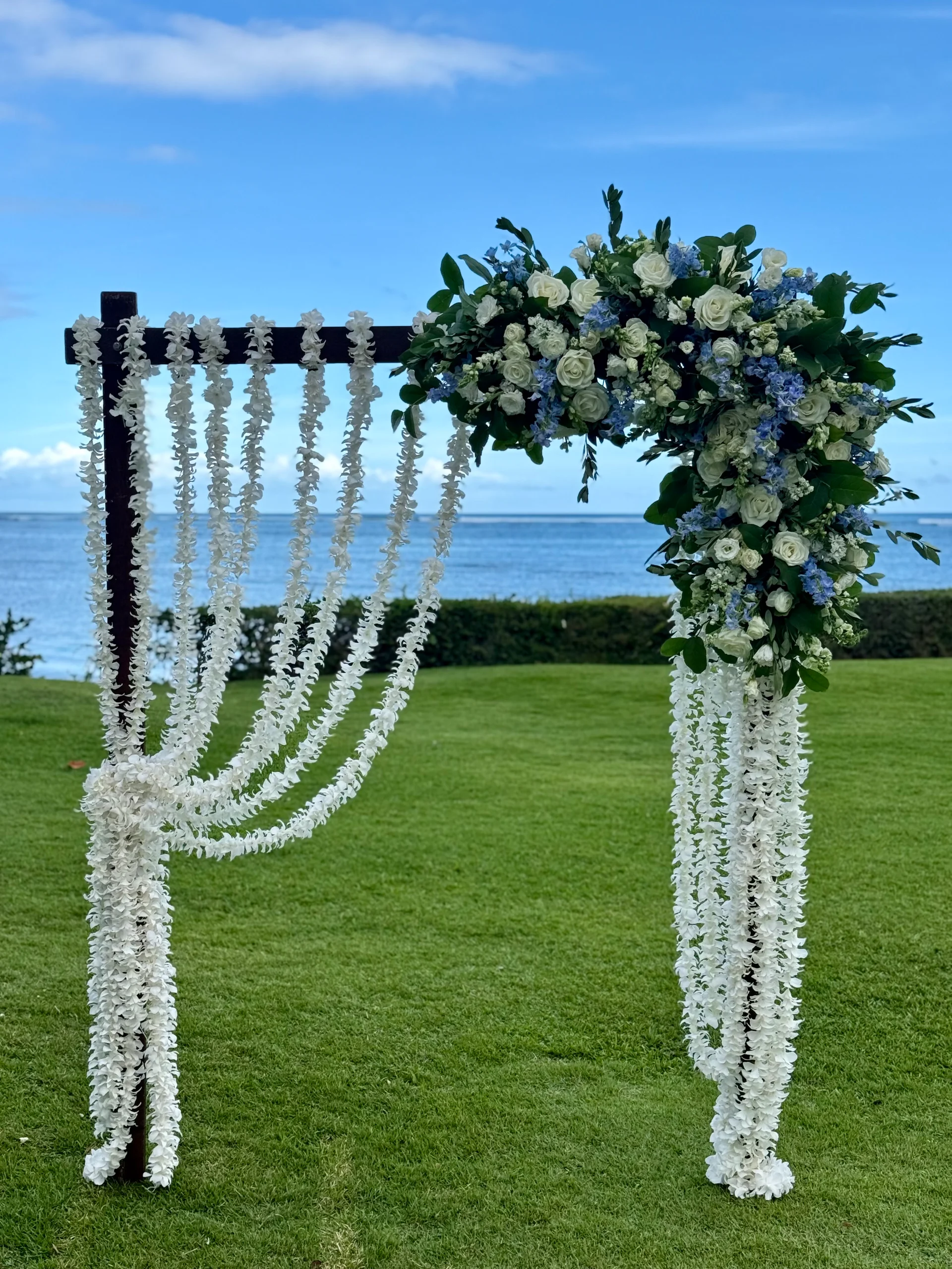beachside wedding arch on Oʻahu decorated with white floral garlands and an arrangement of white and blue flowers