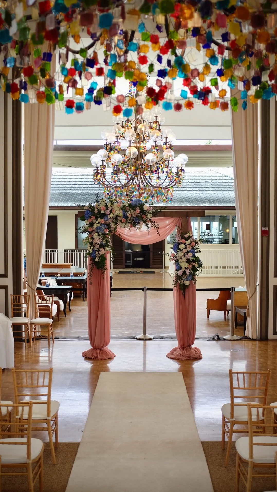 luxurious indoor wedding arch with pink drapes, floral arrangements, and chandelier in Oʻahu venue