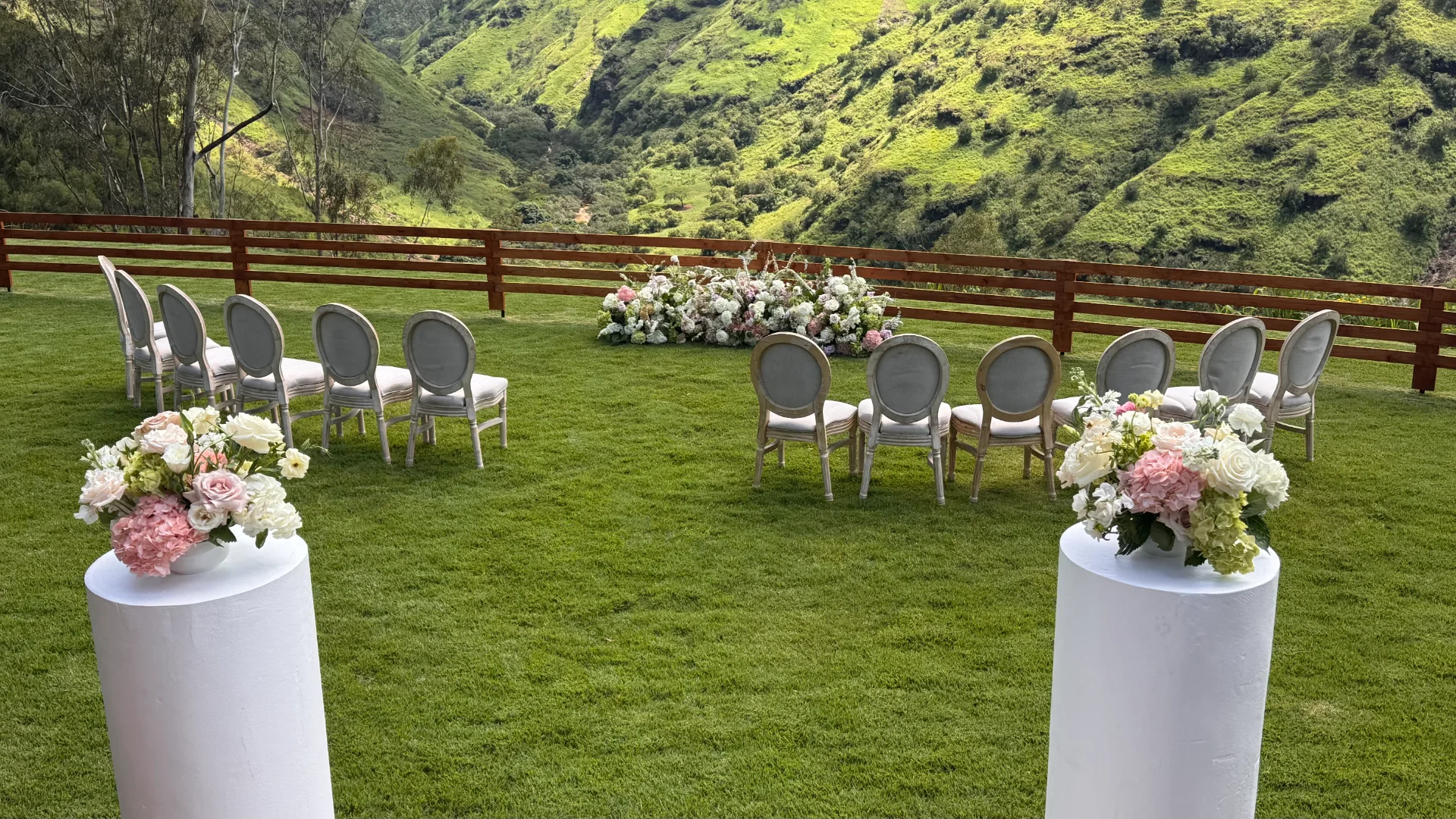 Elegant outdoor wedding setup on lush grass with white and pink hydrangeas and roses on pedestals on Oʻahu.
