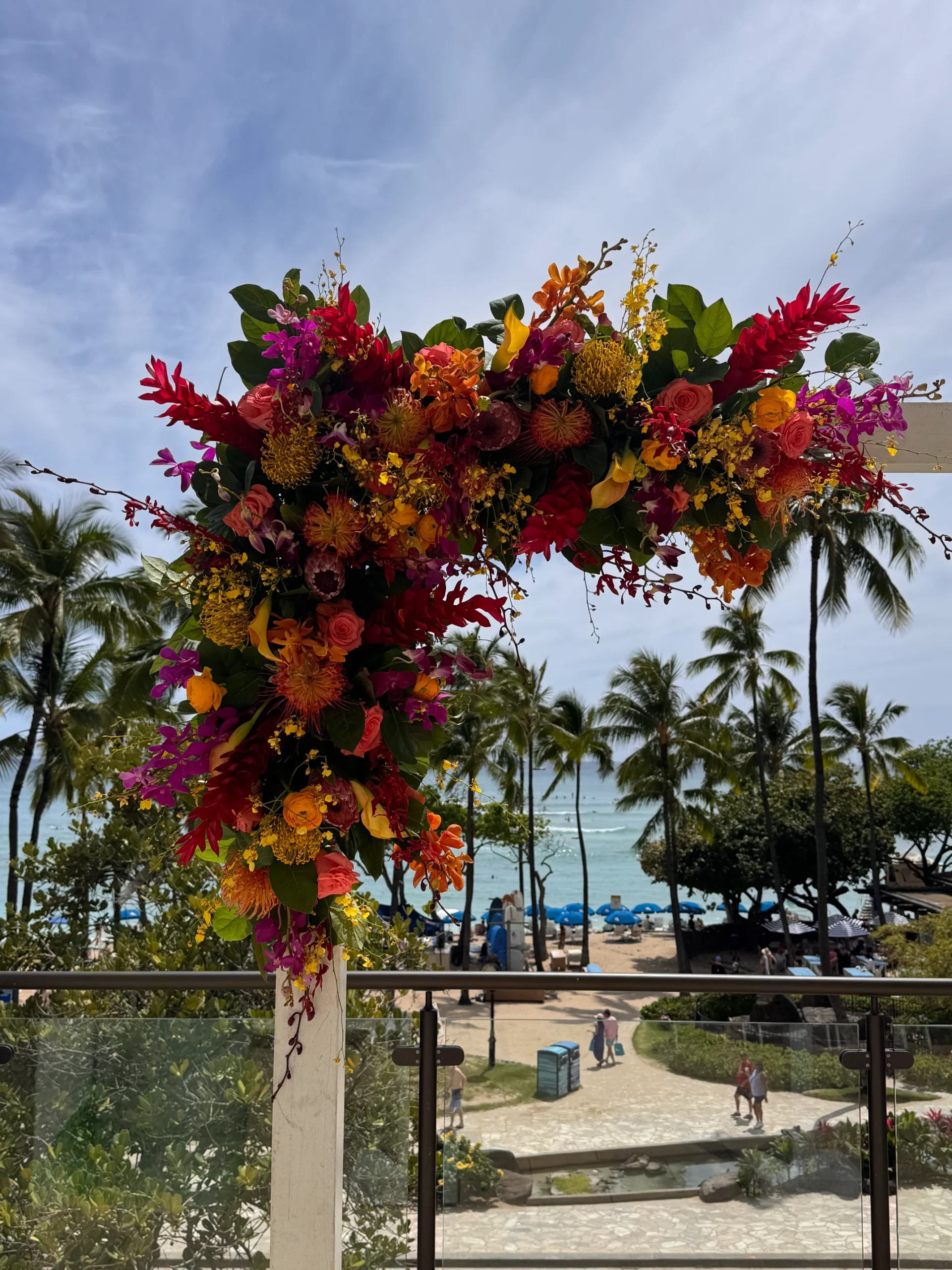 Vibrant tropical wedding floral arrangement with red, orange, and yellow blooms on Oʻahu beachside venue.