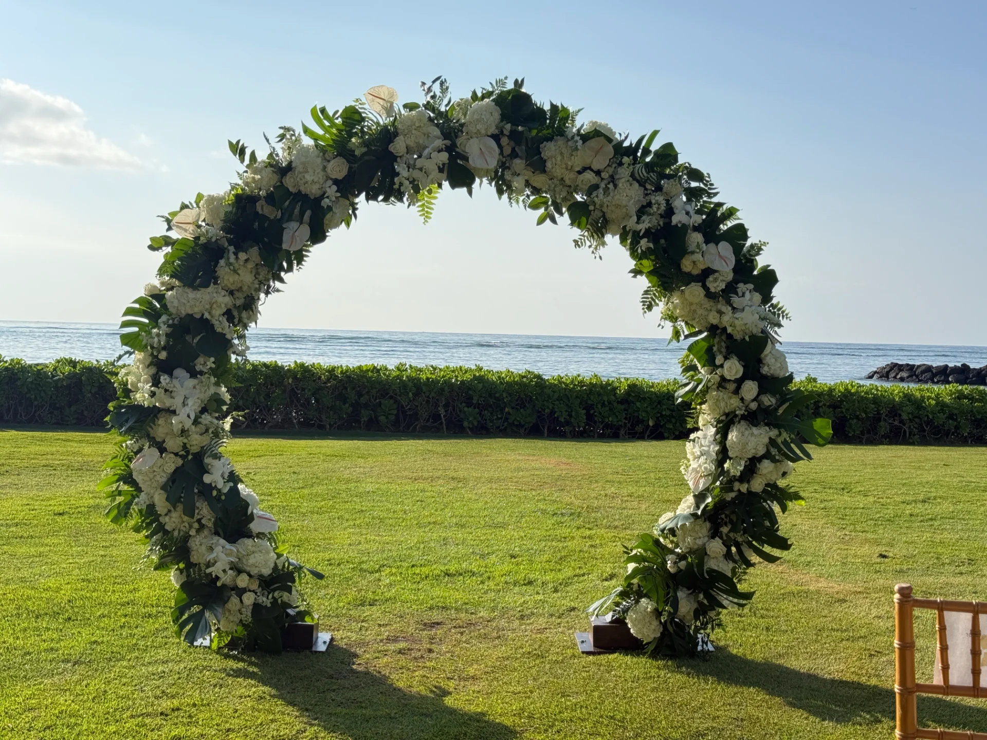 circular floral arch with white flowers and greenery on grassy oceanfront lawn in Oʻahu, Hawaii