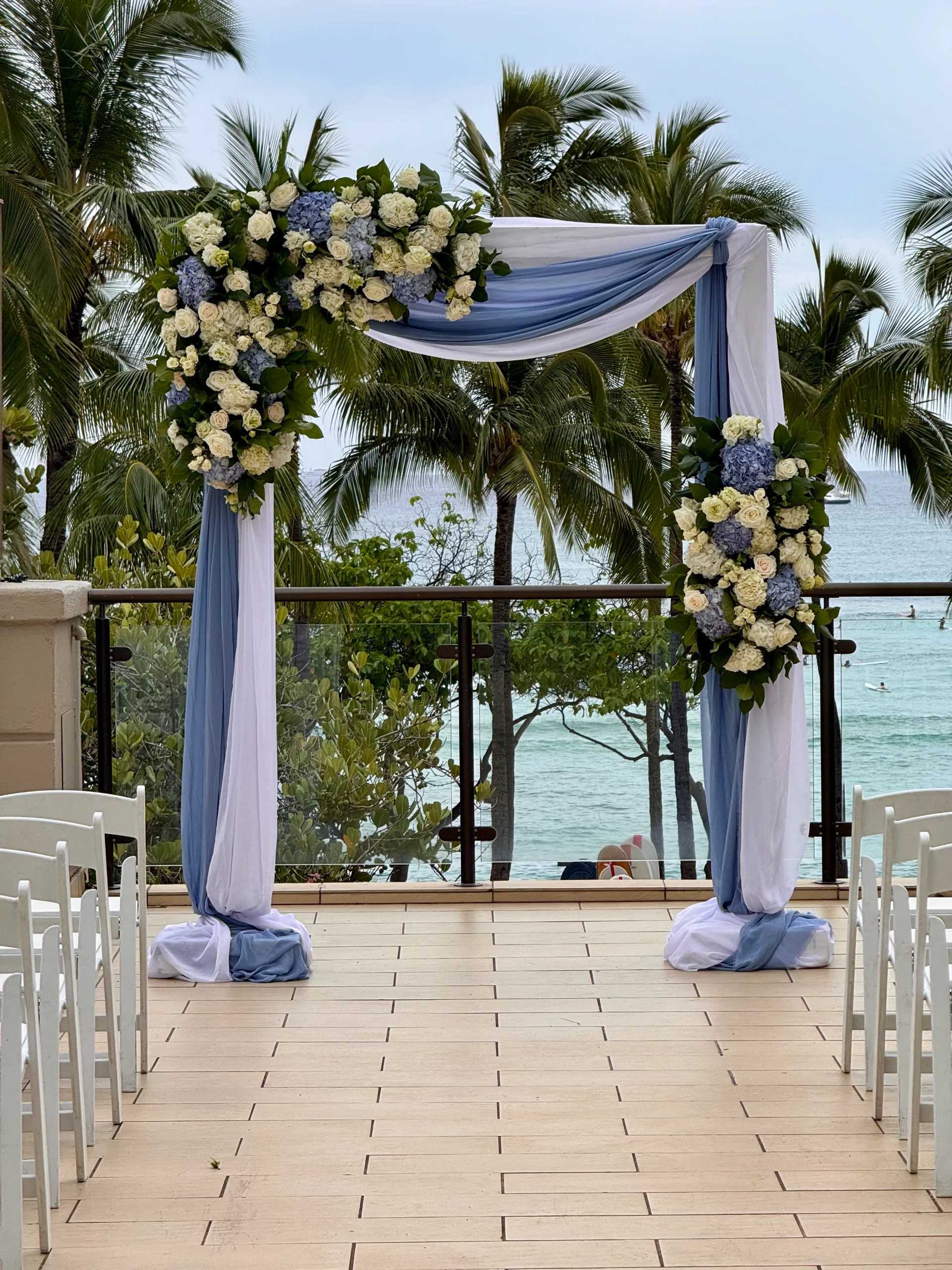 Hawaii beach wedding arch with white and blue flowers and drapery on wooden deck with ocean view