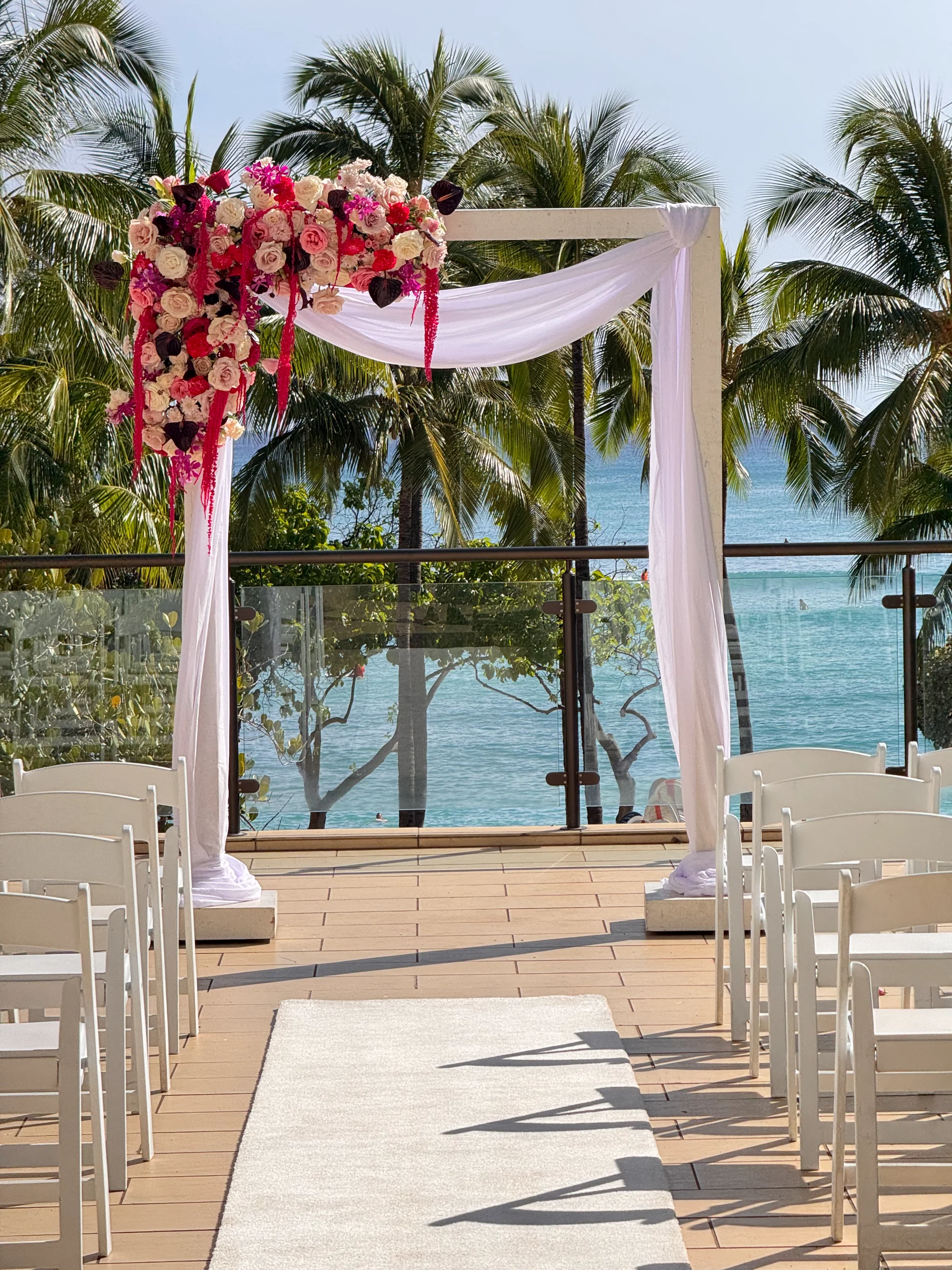 Elegant floral wedding arch with pink and white roses overlooking ocean at beachfront venue in Oʻahu, Hawaii.