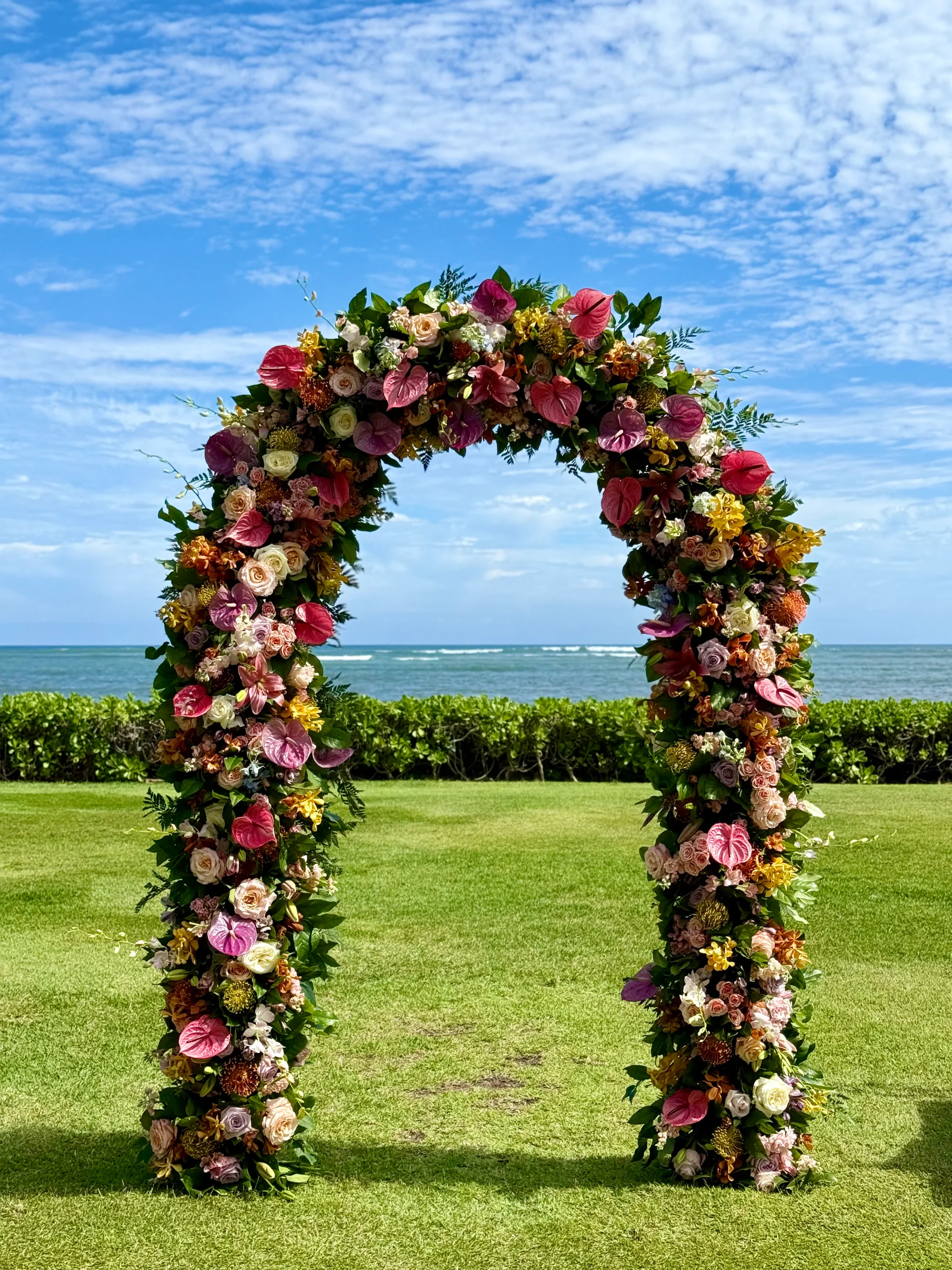 Floral wedding arch with pink anthuriums and roses set against the ocean backdrop at a Hawaii beach venue.