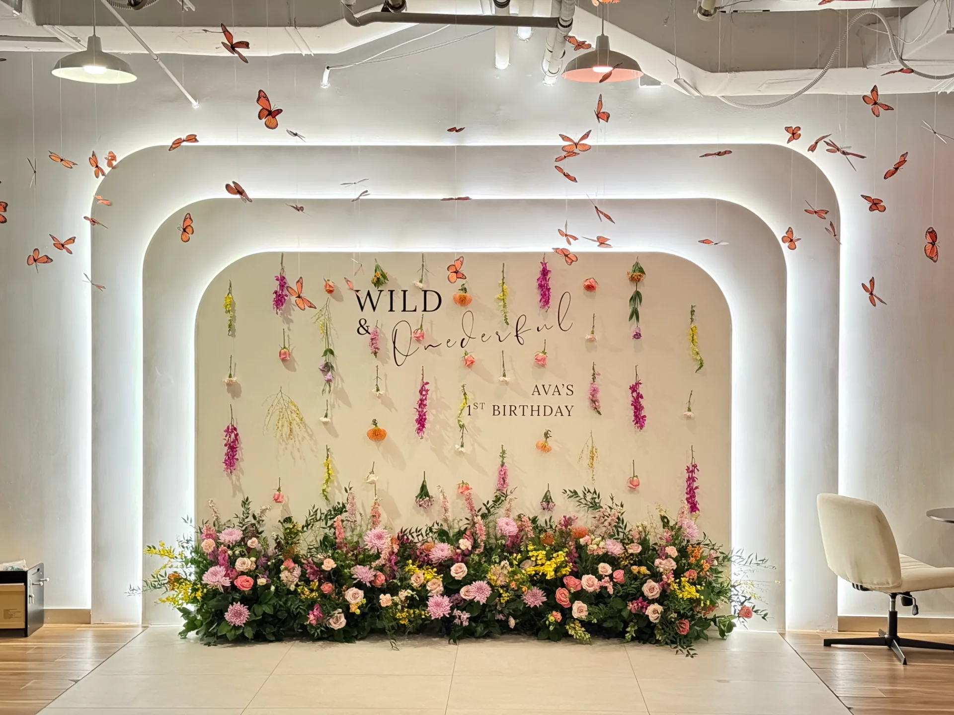 Colorful birthday backdrop with hanging flowers, butterflies, and lush floral arrangement with pink, yellow, and white blooms on Oʻahu.