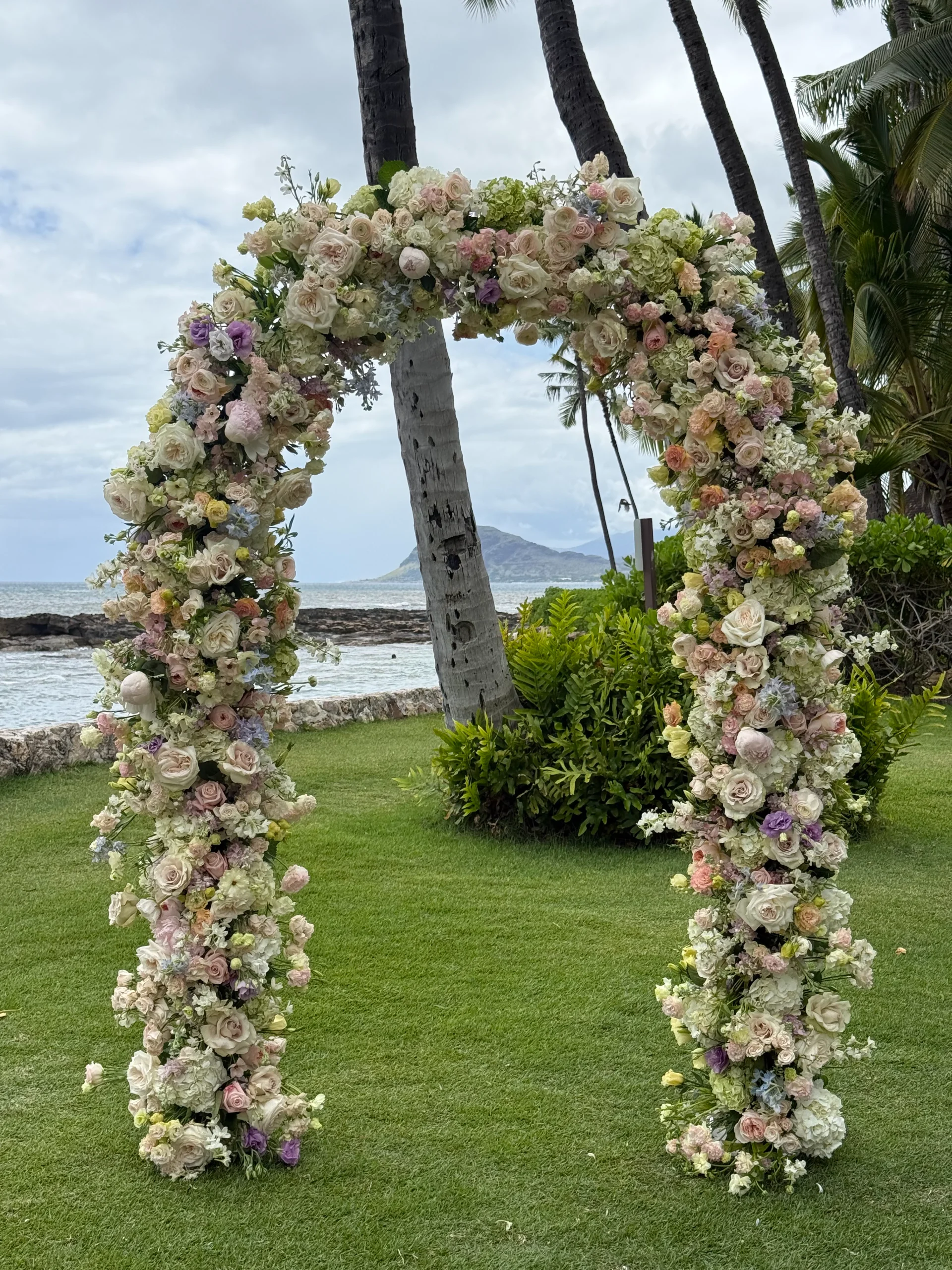 luxurious floral wedding arch with pastel roses and hydrangeas on a lawn overlooking the ocean in Oʻahu, Hawaii