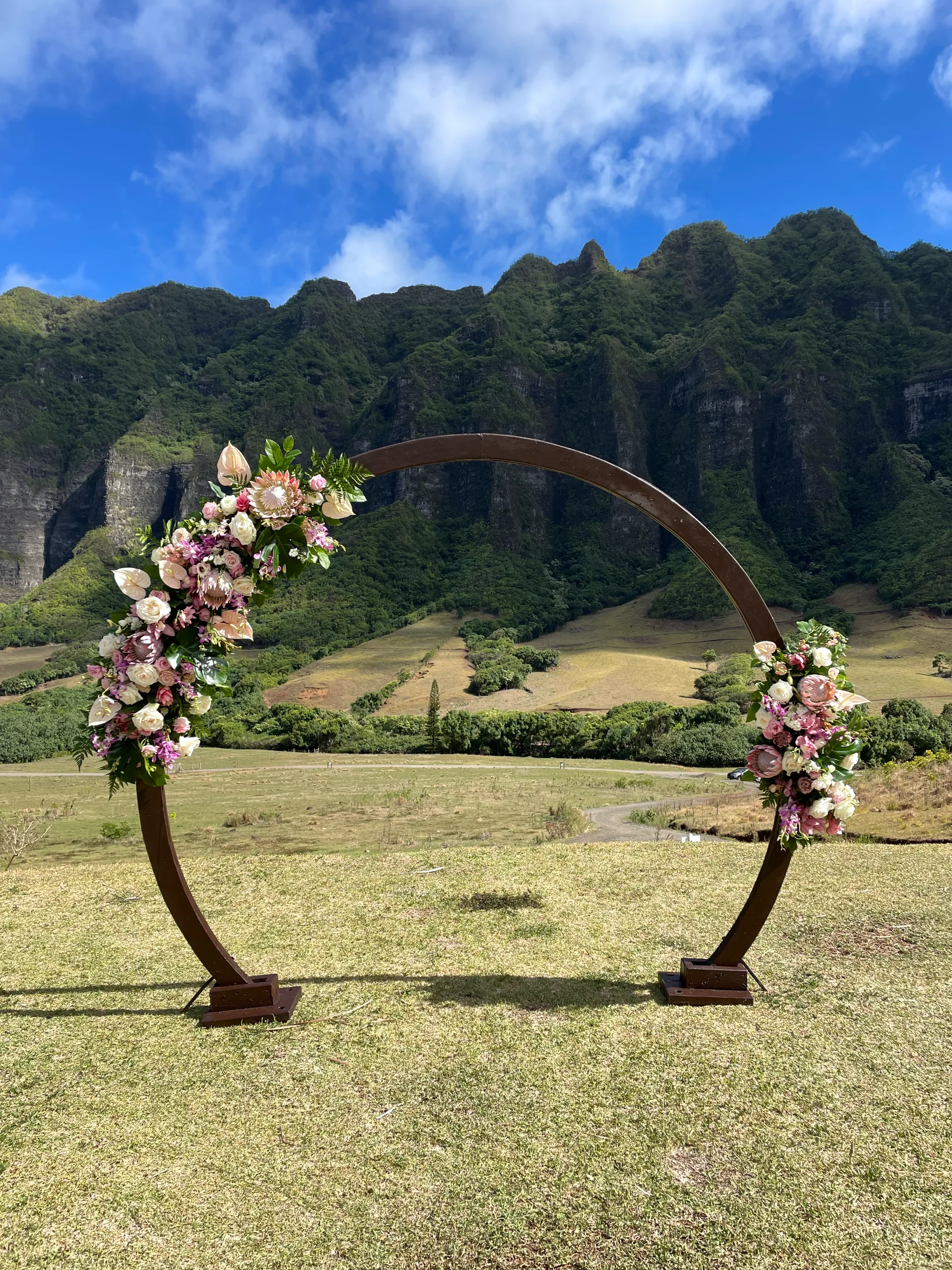 circular wedding arch adorned with pink and white flowers in front of lush Oʻahu mountains