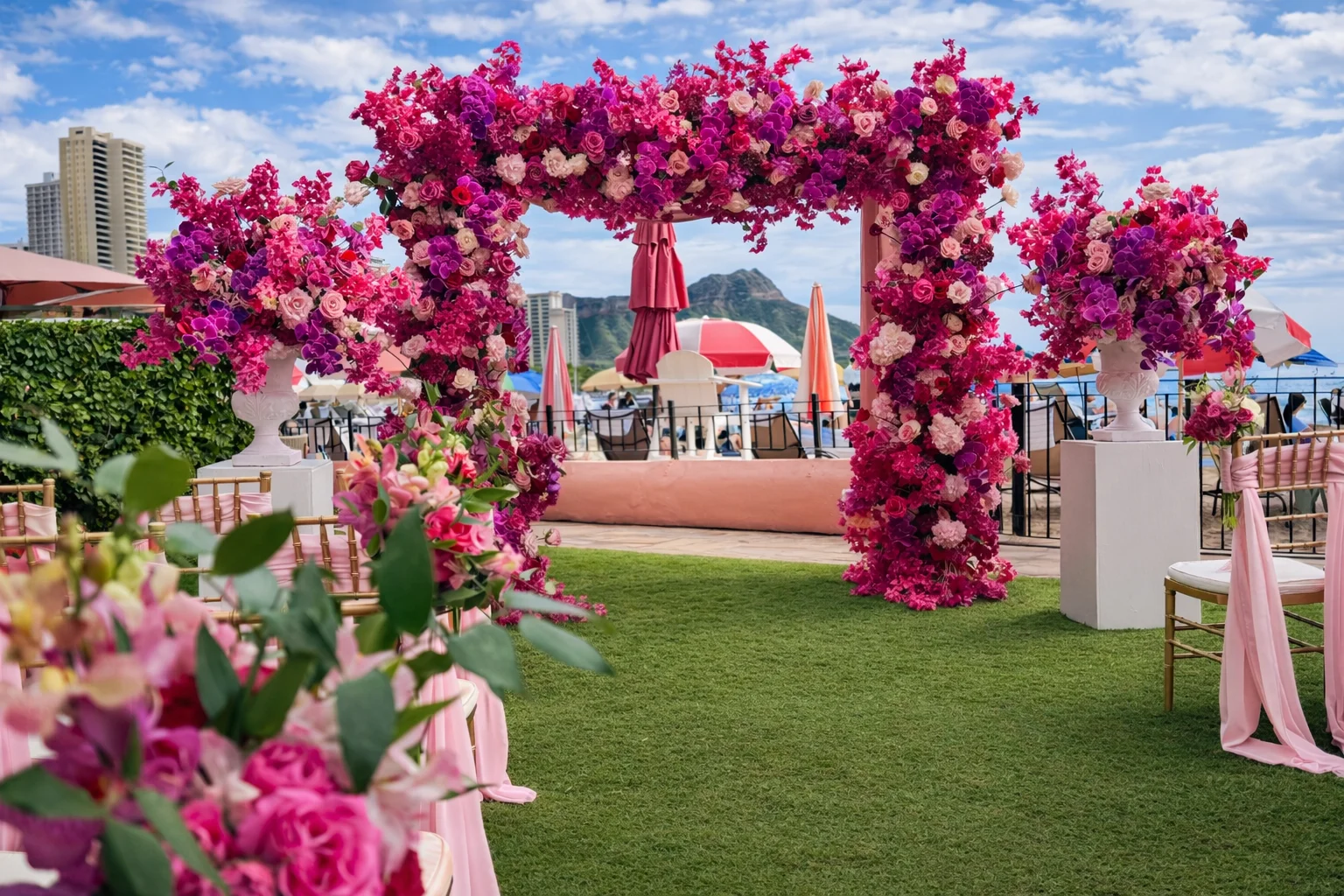 Luxurious pink and magenta flower arch with roses and orchids on Oʻahu beach wedding setting with ocean and city view