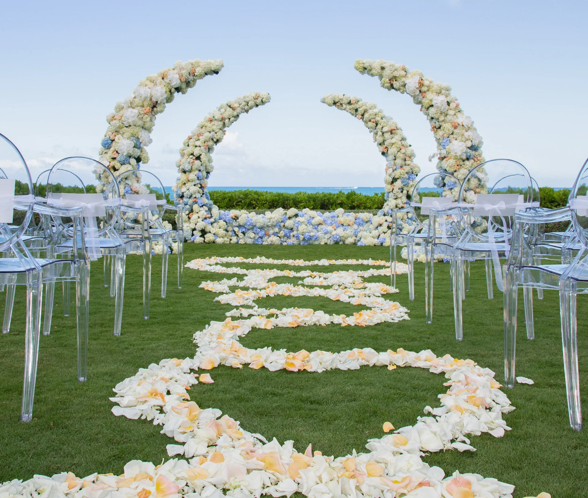 elegant outdoor wedding setup with crescent moon floral arches and aisle of rose petals on lush lawn in Oʻahu