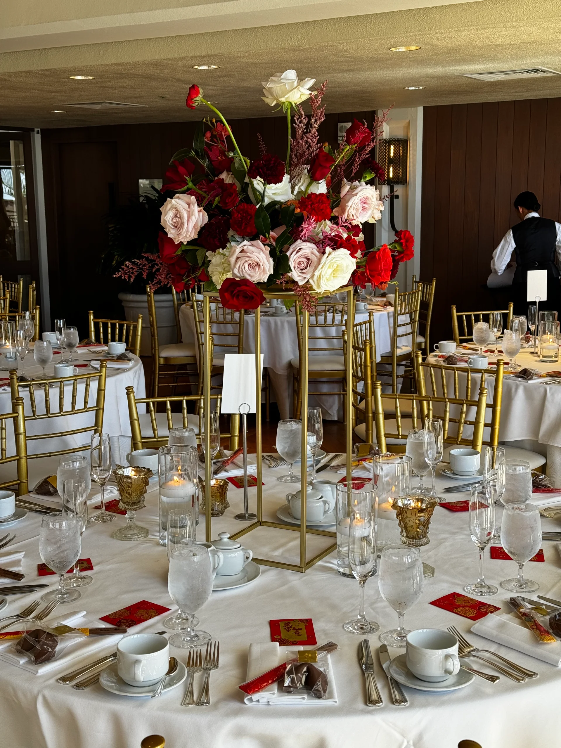 Elegant Oʻahu wedding reception with a tall centerpiece featuring red and pink roses and gold chairs around a white-clothed table