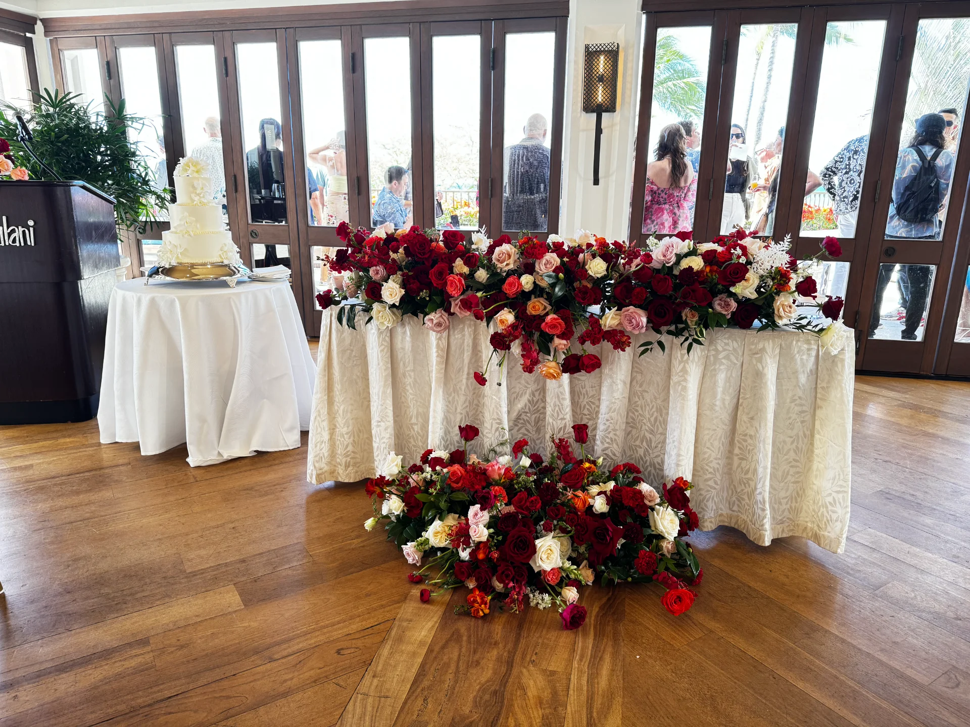 Elegant wedding reception with red and pink floral arrangements on white tablecloth in Oʻahu, Hawaii venue.