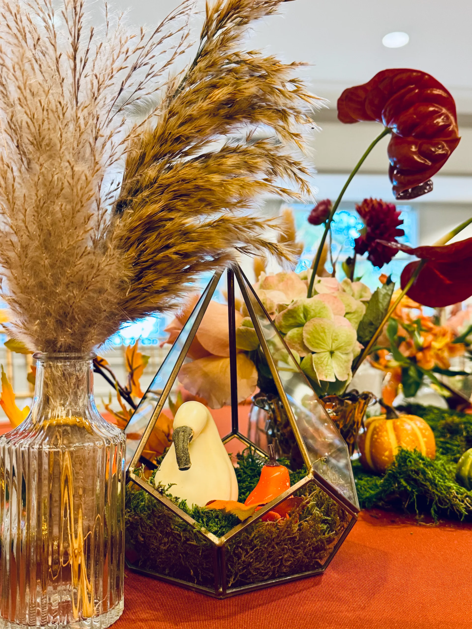 Oʻahu wedding reception table with pampas grass in a glass vase, glass terrarium with ceramic bird, and autumnal florals.