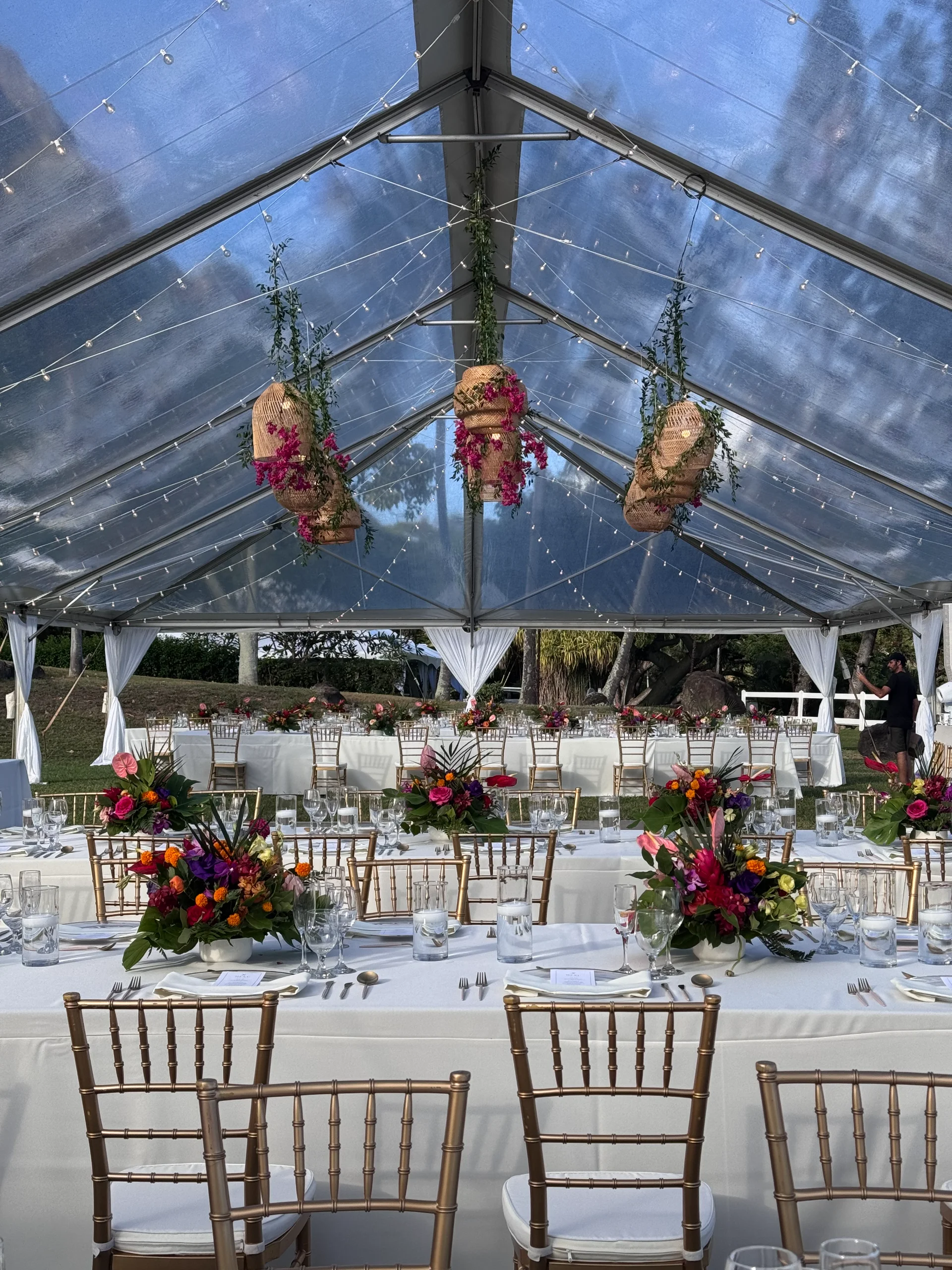 elegant wedding reception with vibrant florals and gold chairs under a clear tent on Oʻahu