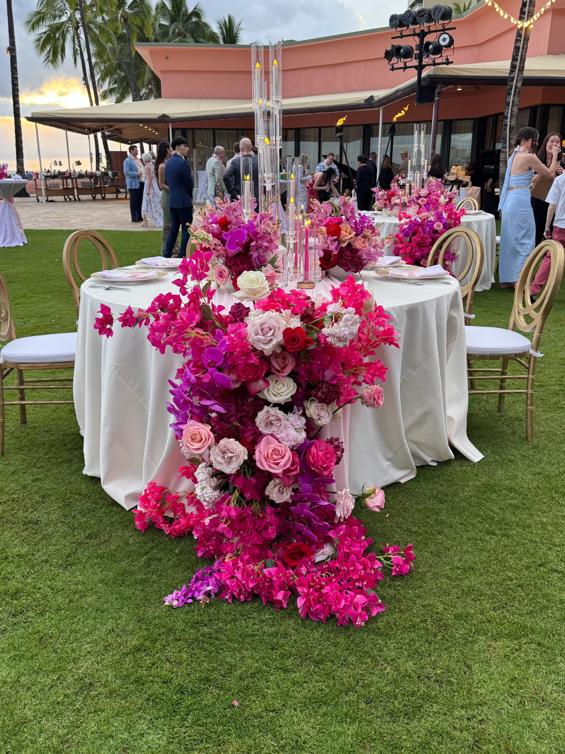 Elegant outdoor wedding reception on Oʻahu with luxurious pink and magenta floral arrangements cascading from tables.