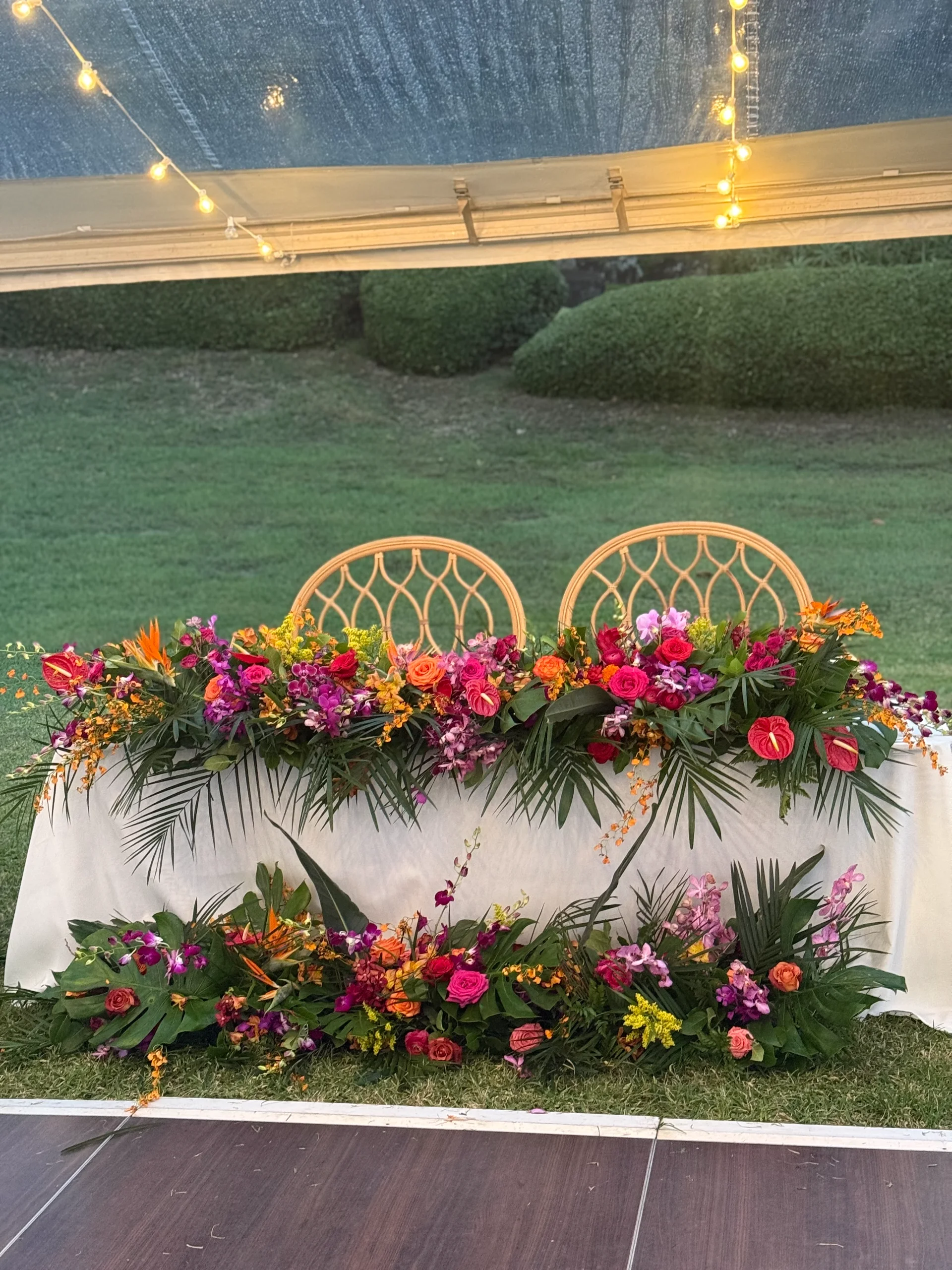 Luxurious wedding reception table with vibrant tropical florals including pink, orange, and purple blooms under a tent in Oʻahu.