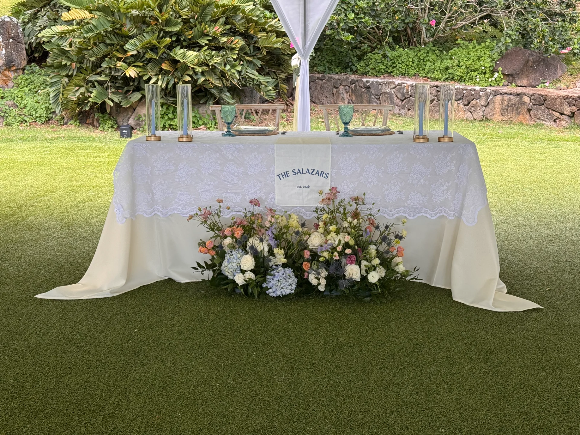Elegant wedding reception table with lush floral arrangement featuring roses, hydrangeas, and greenery on Oʻahu
