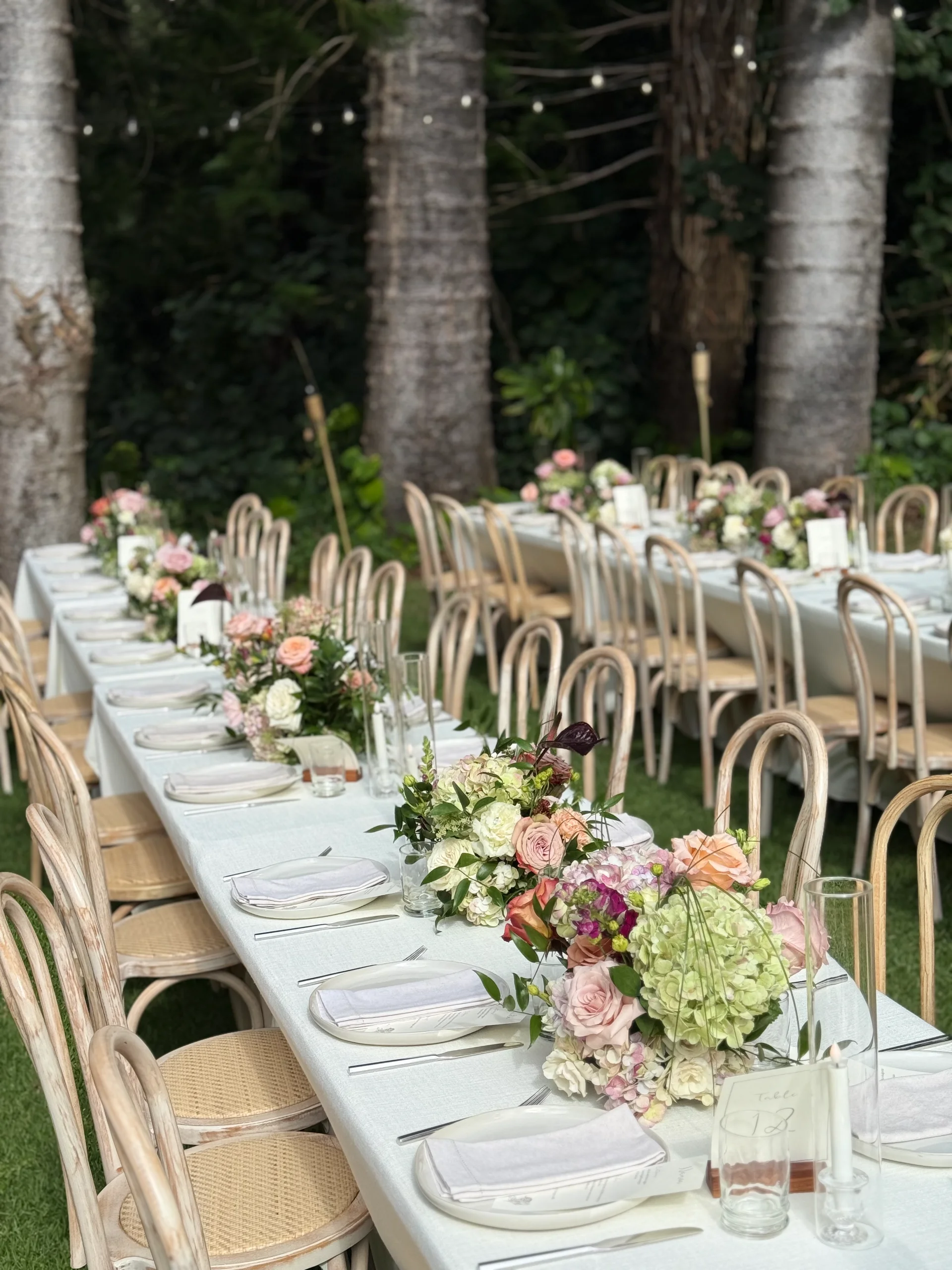 Elegant outdoor wedding reception on Oʻahu with white tablecloths and lush floral centerpieces featuring roses and hydrangeas.