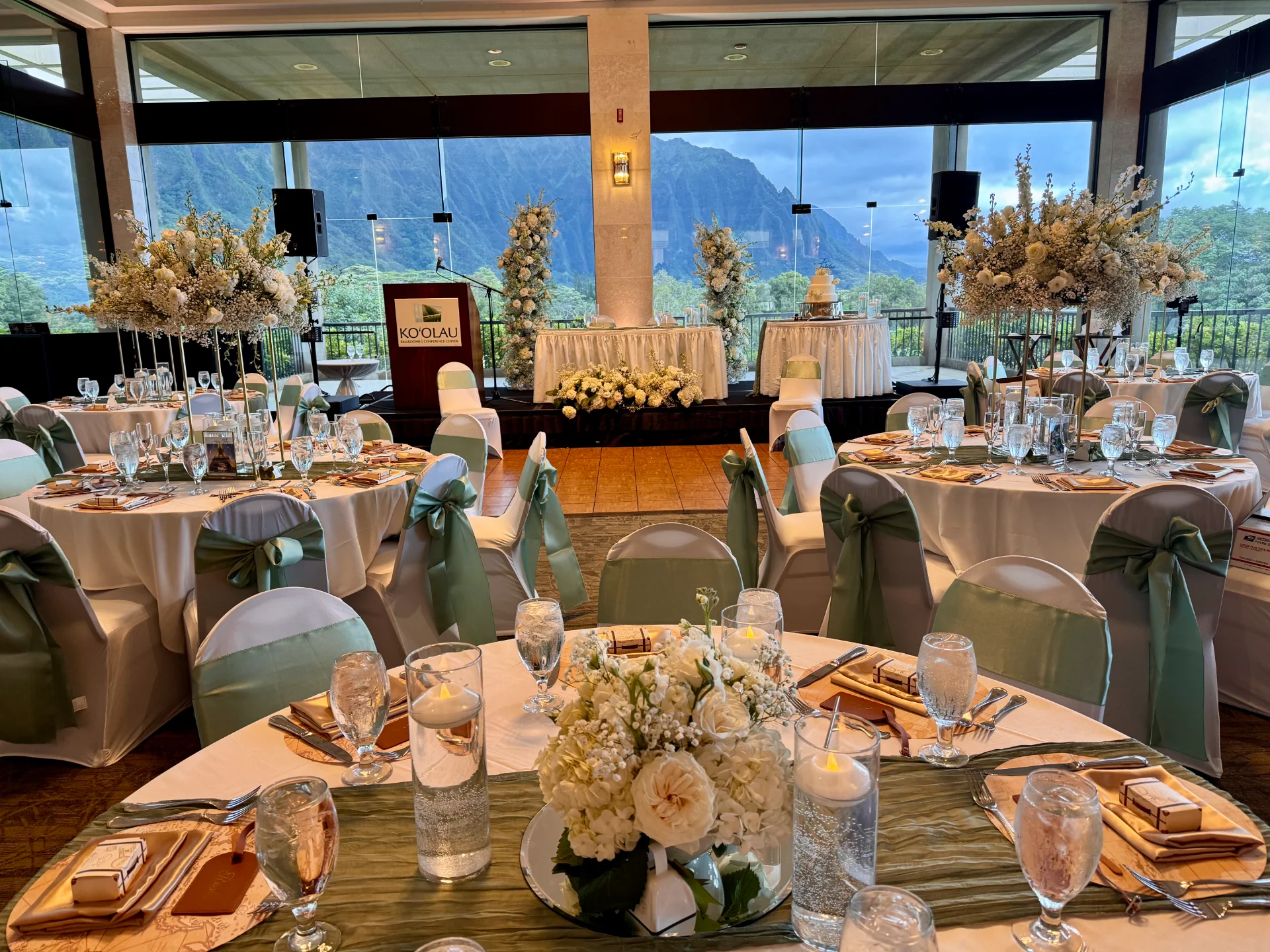 Elegant wedding reception with white roses and greenery centerpieces at Koʻolau, Oʻahu, with mountain views.