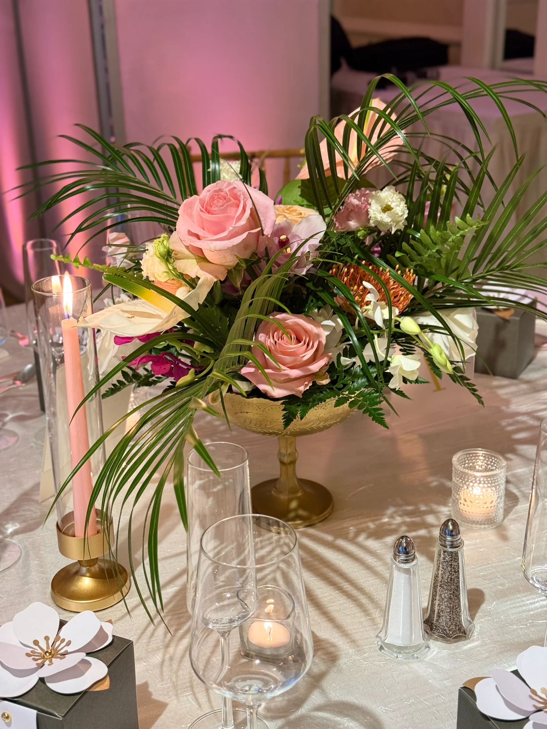 Elegant centerpiece with pink roses, palm leaves, and candles on a decorated wedding table in Hawaii