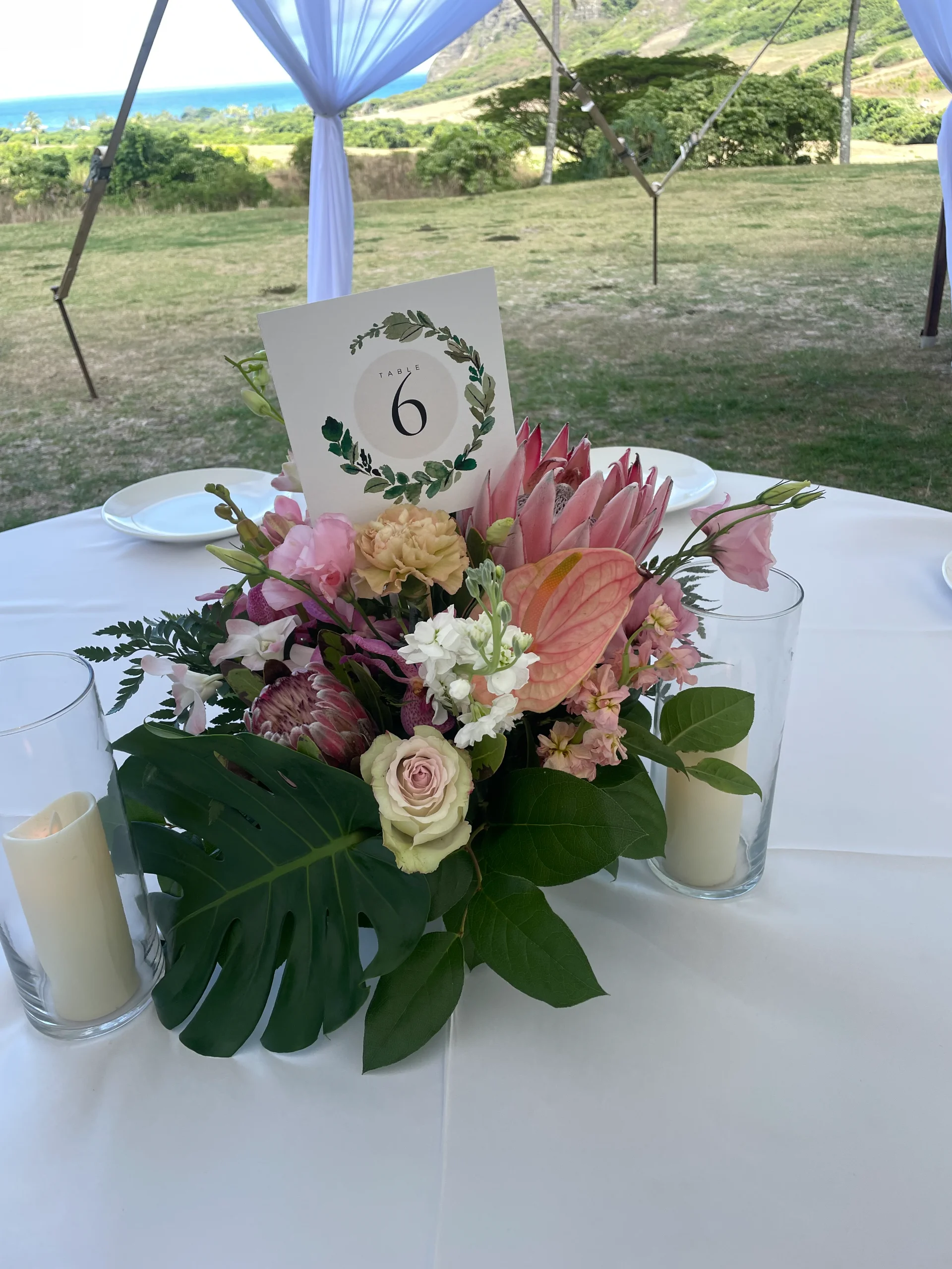 Elegant centerpiece with pink protea, roses, anthuriums, surrounded by greenery on a table at a Hawaii wedding reception.