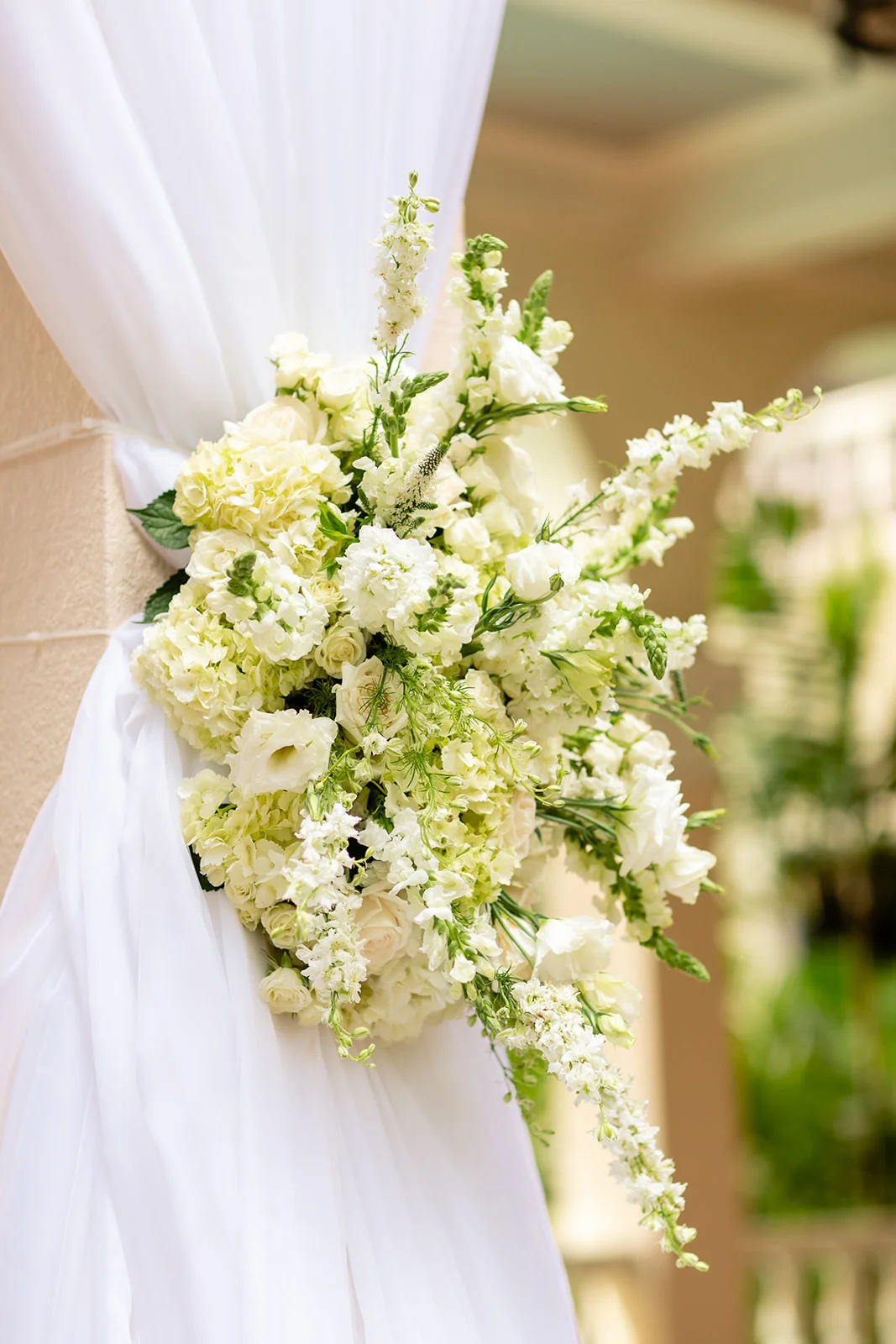 Elegant white and cream floral arrangement with roses and hydrangeas on draped fabric at Cafe Julia wedding, Oʻahu.