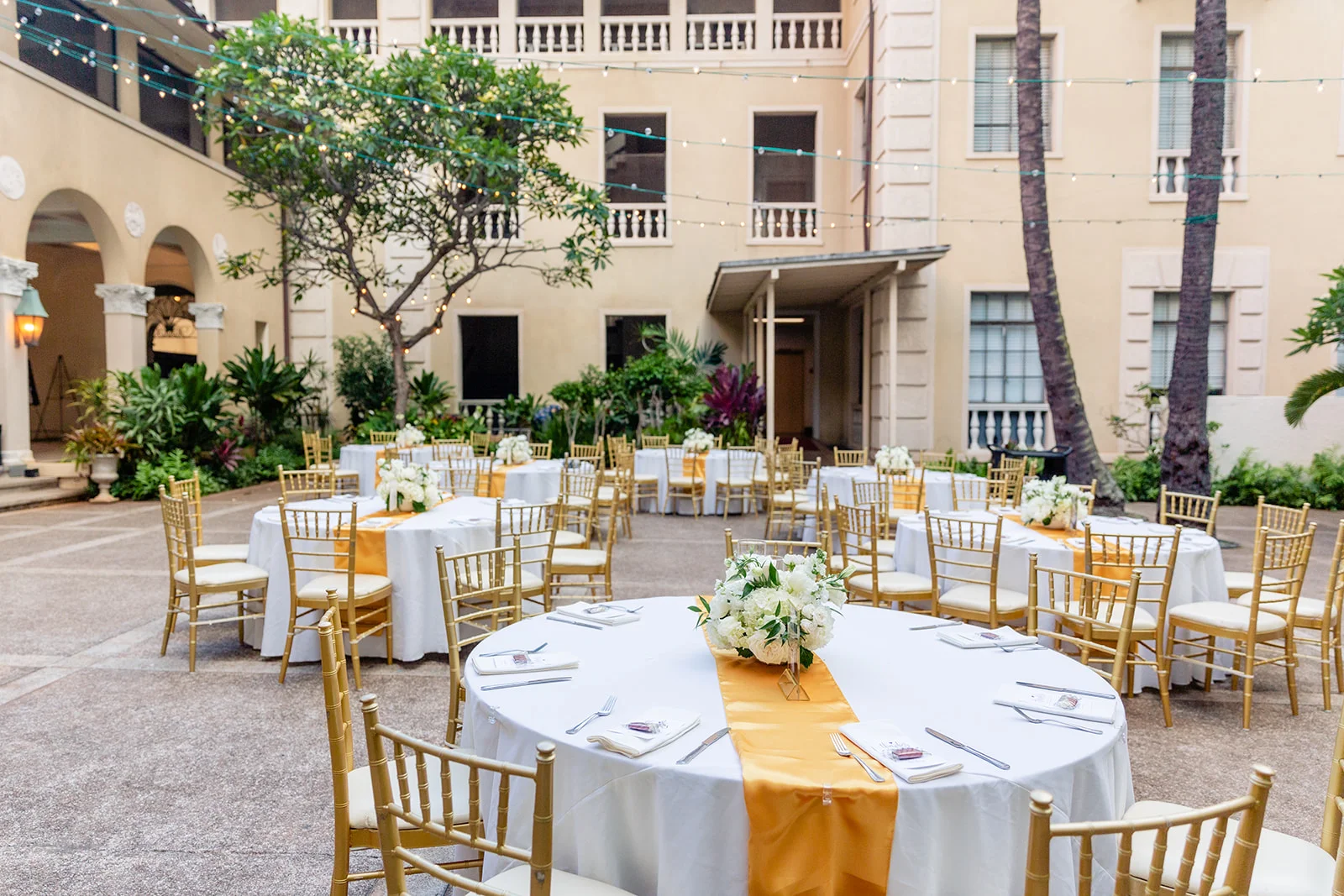Luxury wedding setup at Cafe Julia, Oʻahu with white floral centerpieces, gold chiavari chairs, and yellow table runners