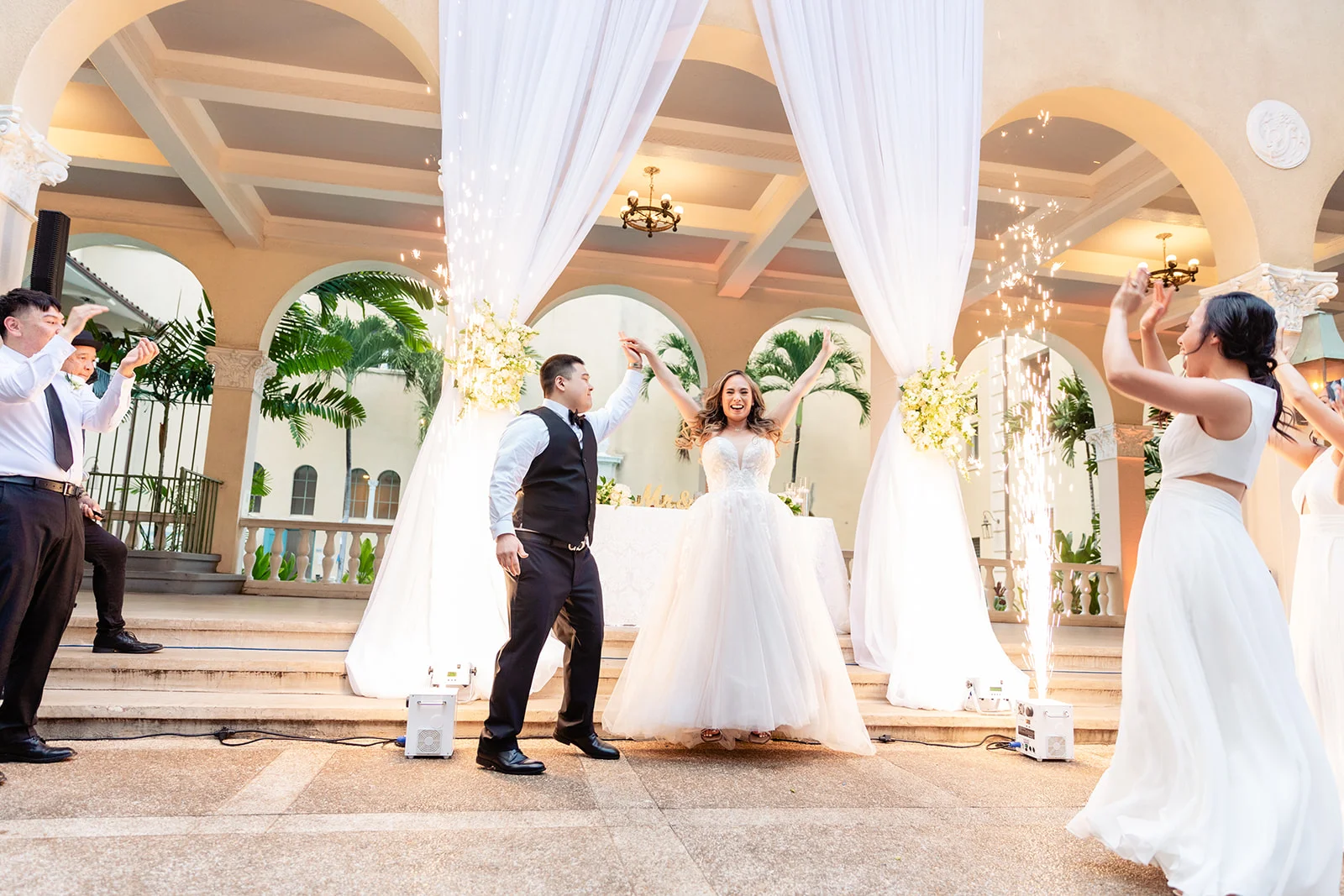 Bride and groom celebrating at Cafe Julia with white drapery, floral arrangements, and sparklers in an Oʻahu wedding setting.
