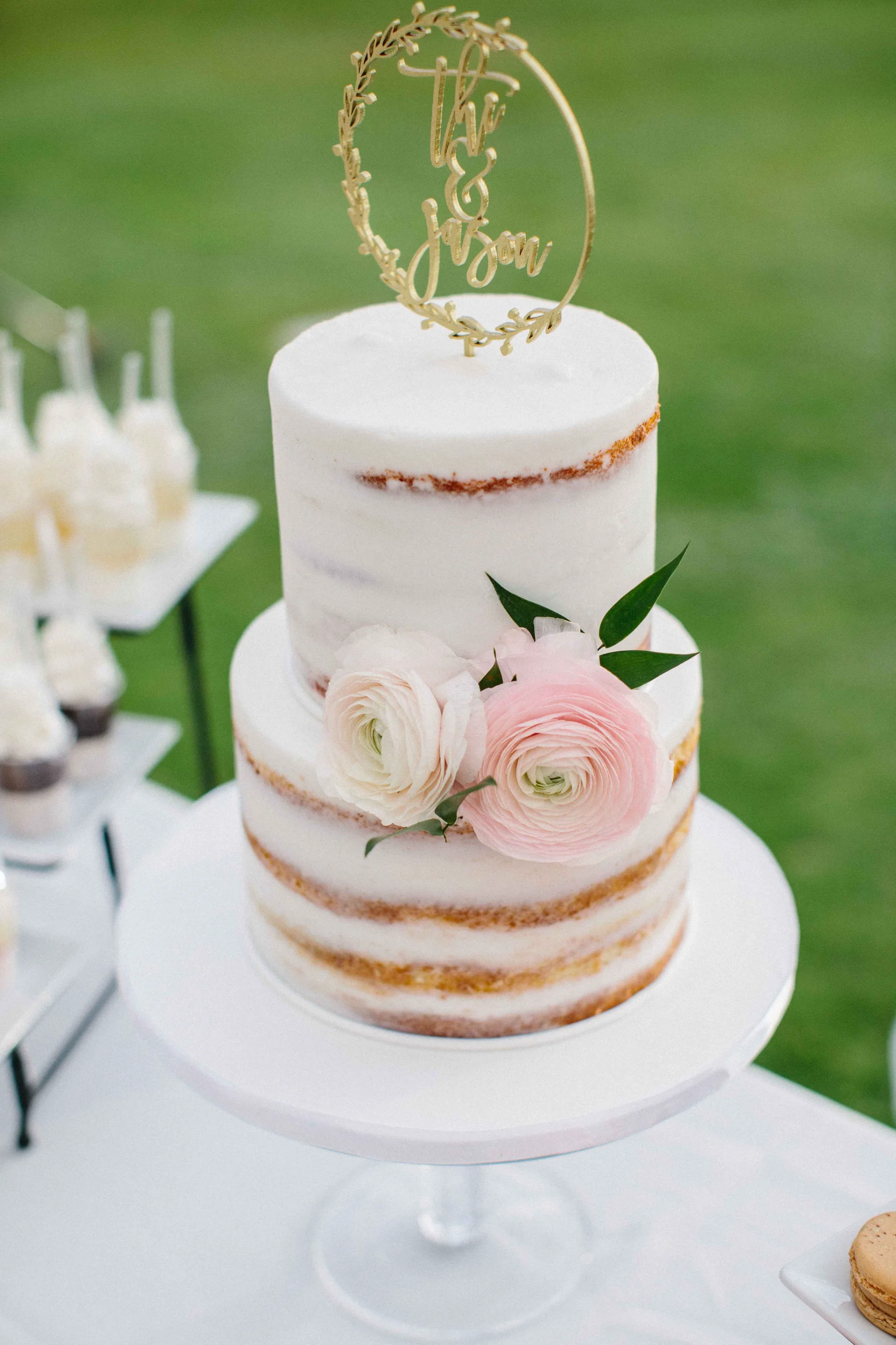 Elegant two-tier semi-naked wedding cake with delicate pink and white ranunculus flowers at Lanikūhonua Cultural Institute, Oʻahu.