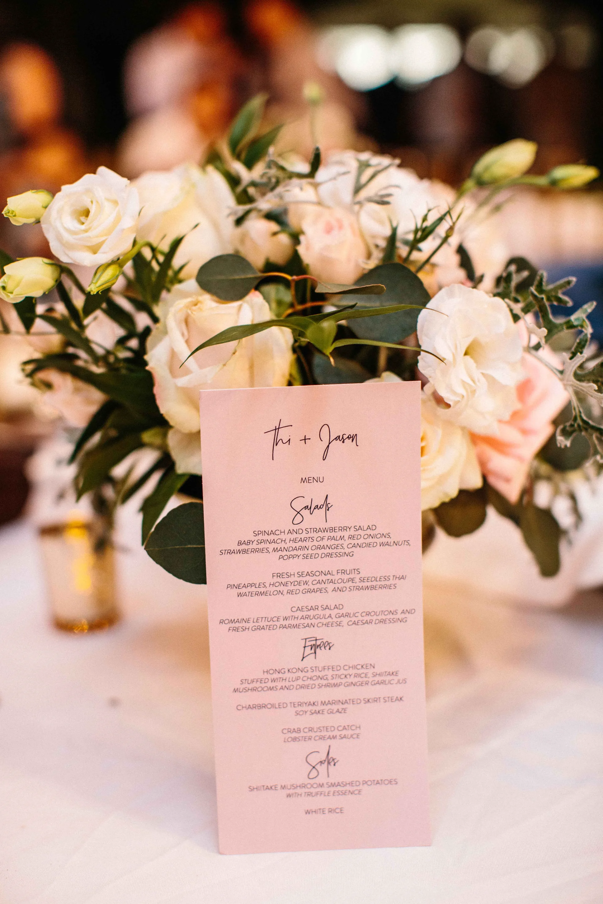 Elegant table centerpiece with white roses and greenery at Lanikūhonua wedding, accompanying a pink menu.