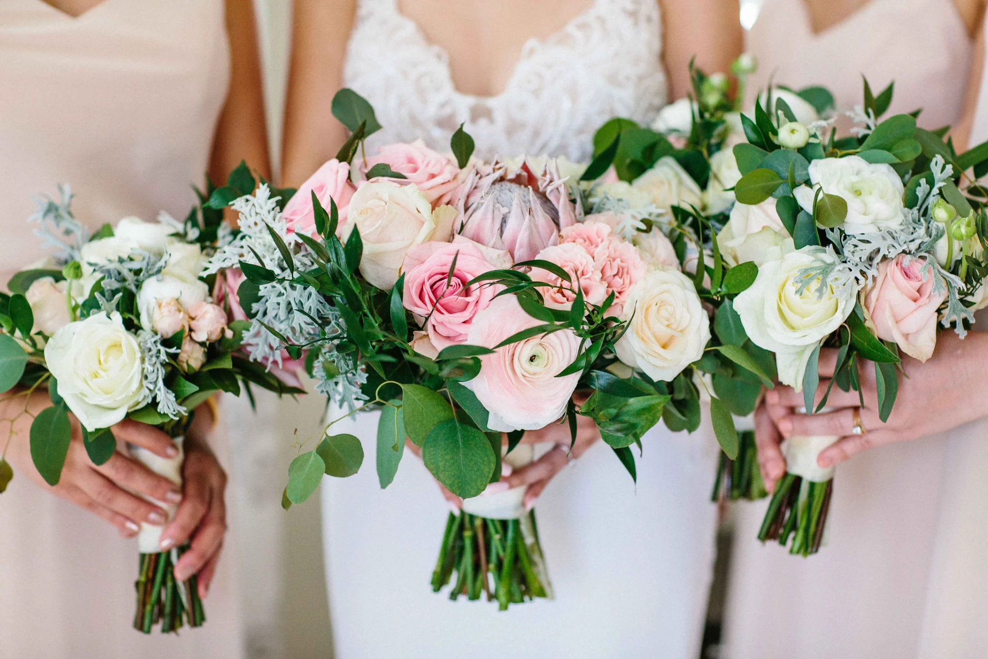 Bridesmaids holding elegant bouquets with pink and white roses, greenery, and protea at Lanikūhonua Cultural Institute, Oʻahu.