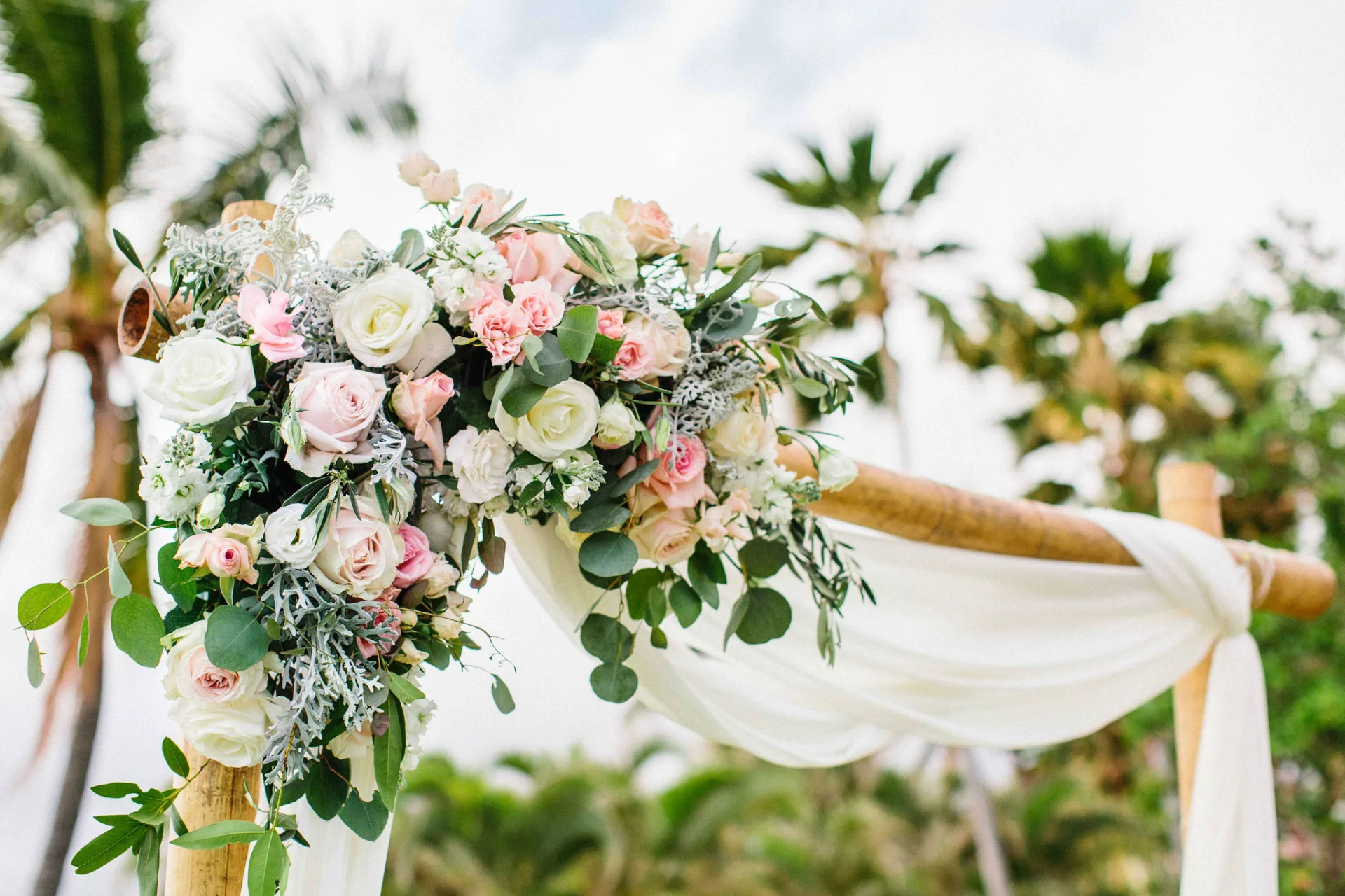 Elegant floral arch with white and pink roses against palm trees at Lanikūhonua Cultural Institute wedding on Oʻahu